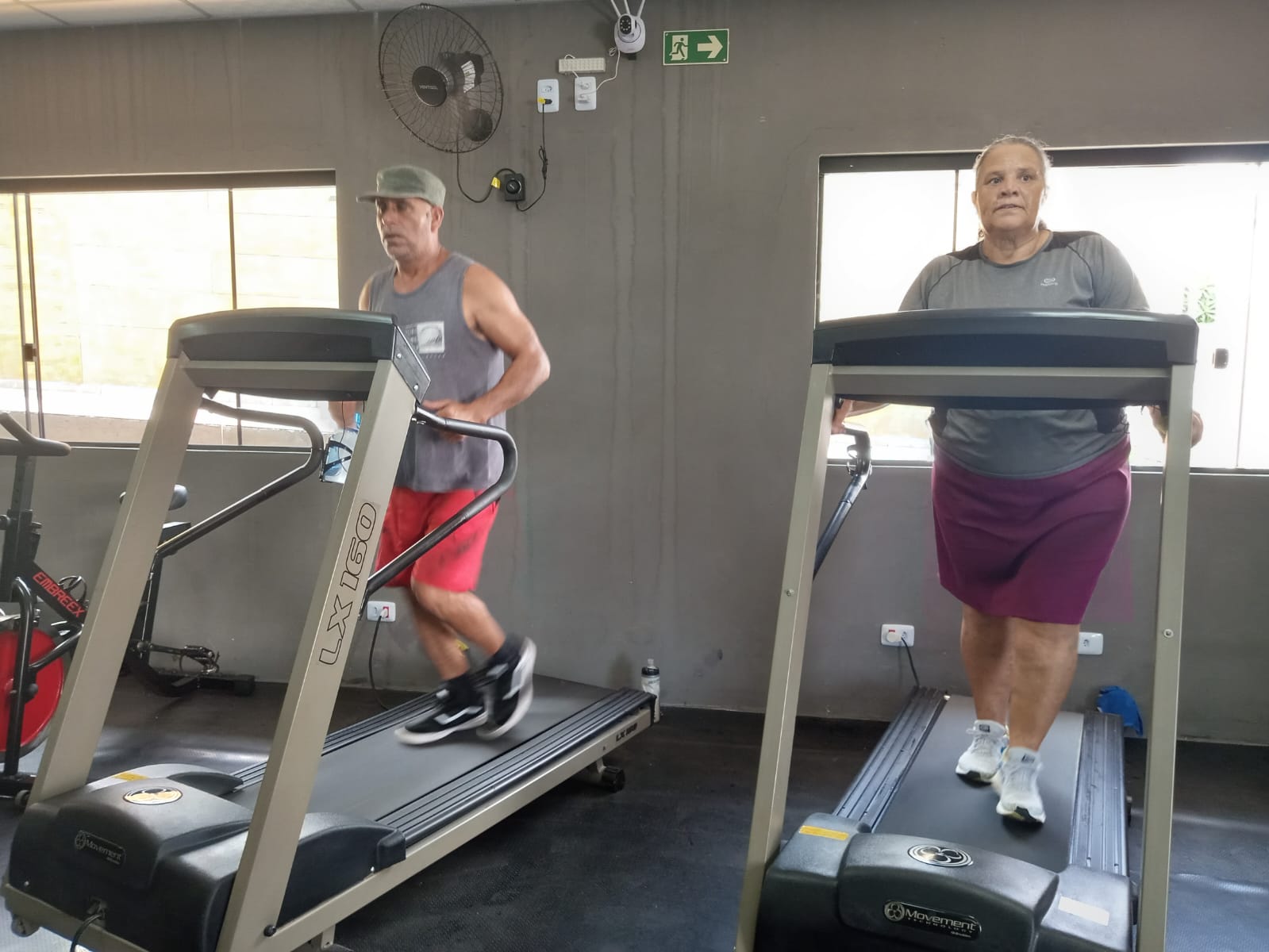 Aluno e aluna treinando lado a lado nas esteiras da academia do Js Team Personal