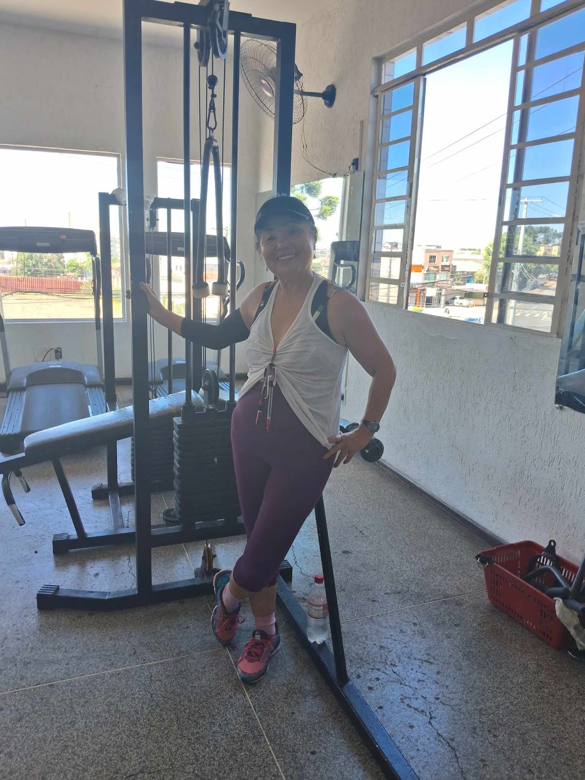 Aluna sorridente ao lado do aparelho de musculação, durante o treino